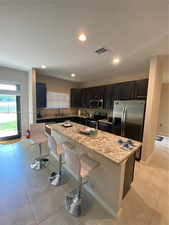 kitchen with a breakfast bar area, stainless steel appliances, a center island, and light stone countertops