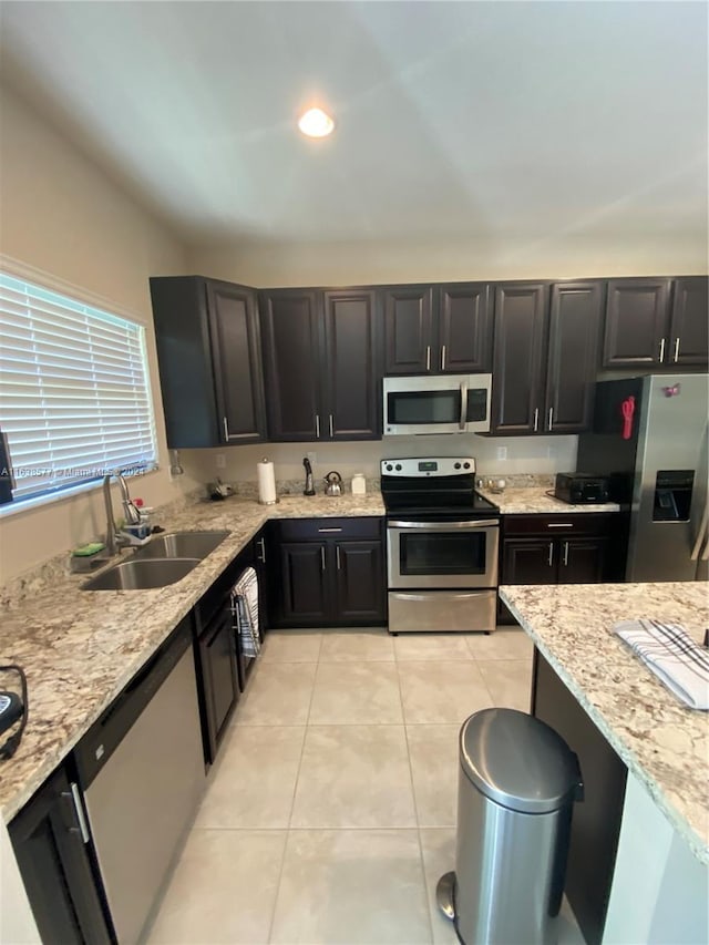 kitchen with appliances with stainless steel finishes, sink, light tile patterned floors, and light stone countertops