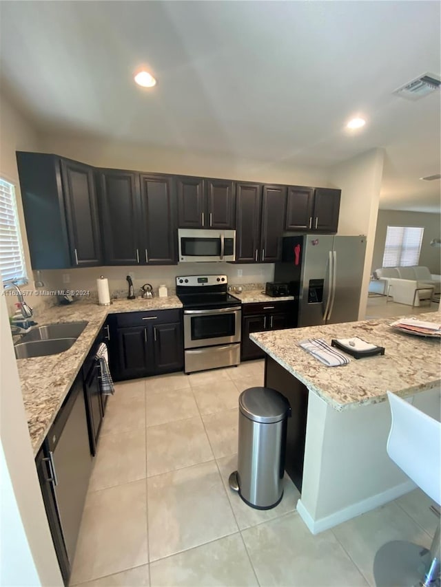 kitchen featuring appliances with stainless steel finishes, light tile patterned floors, sink, and light stone countertops