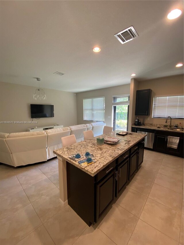 kitchen featuring light tile patterned flooring, sink, light stone counters, and a kitchen island