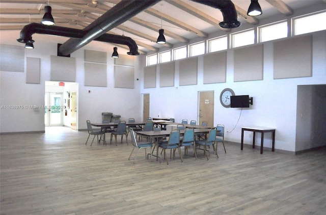 dining space featuring wood-type flooring, beamed ceiling, a towering ceiling, and a healthy amount of sunlight