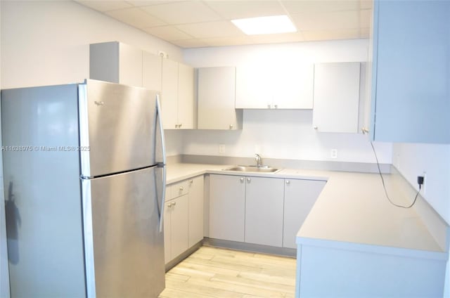 kitchen with sink, light hardwood / wood-style flooring, a paneled ceiling, and stainless steel refrigerator