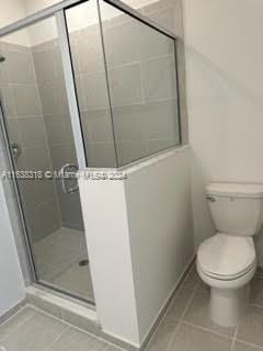 bathroom with walk in shower, toilet, and tile patterned floors