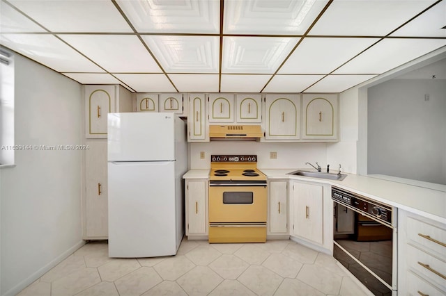 kitchen with light tile patterned flooring, white appliances, sink, and cream cabinets