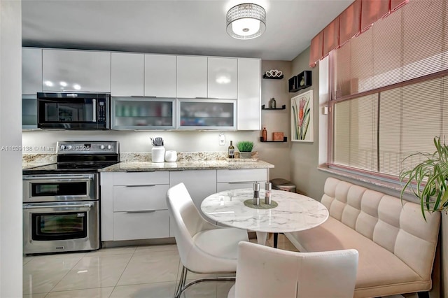 kitchen with light stone countertops, white cabinetry, light tile patterned floors, and range with two ovens