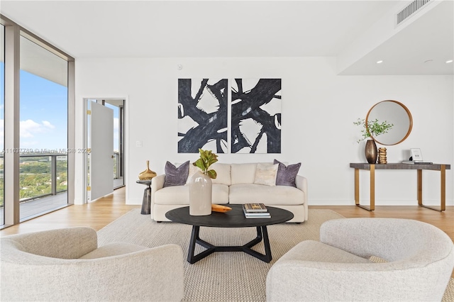 living area with expansive windows, baseboards, visible vents, and wood finished floors