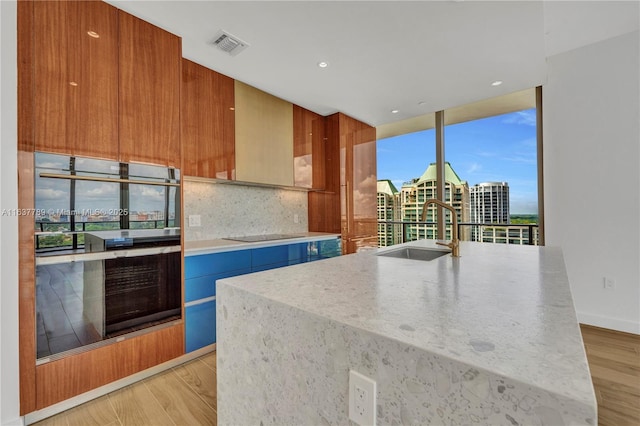 kitchen featuring a center island with sink, double wall oven, sink, decorative backsplash, and light hardwood / wood-style floors