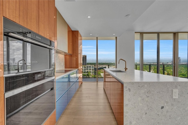 kitchen featuring a wall of windows, light wood-style floors, brown cabinetry, modern cabinets, and a sink