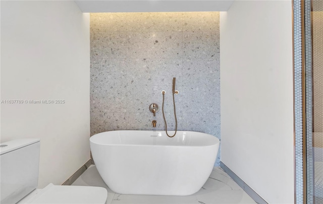 bathroom with toilet, baseboards, marble finish floor, and a freestanding bath