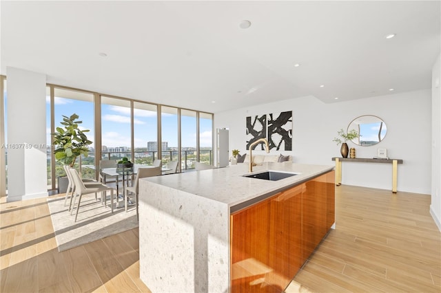 kitchen featuring light stone countertops, floor to ceiling windows, sink, a large island with sink, and light hardwood / wood-style flooring