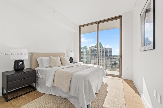 bedroom featuring a view of city, access to outside, expansive windows, wood finished floors, and baseboards