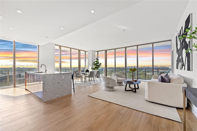 living room featuring floor to ceiling windows, a water view, sink, and light hardwood / wood-style flooring