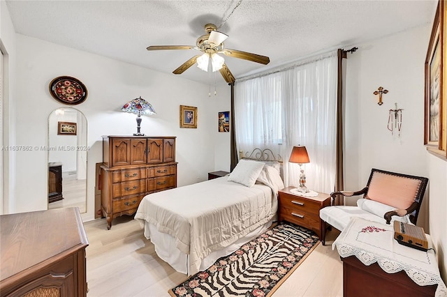 bedroom with a textured ceiling, light wood-type flooring, and ceiling fan