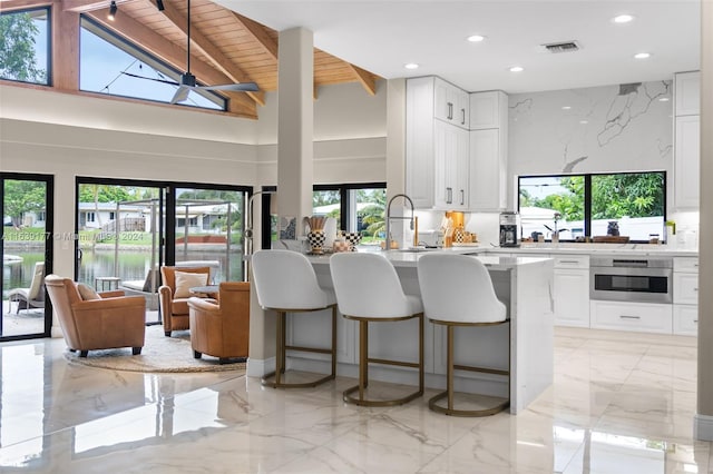 kitchen with a kitchen breakfast bar, a water view, white cabinets, decorative backsplash, and stainless steel oven