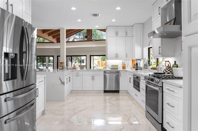 kitchen featuring white cabinetry, appliances with stainless steel finishes, kitchen peninsula, light stone countertops, and wall chimney range hood