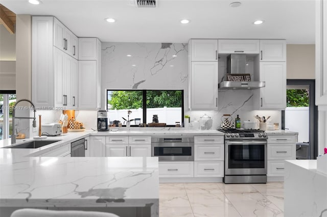 kitchen featuring sink, stainless steel gas range, white cabinetry, light stone counters, and wall chimney exhaust hood