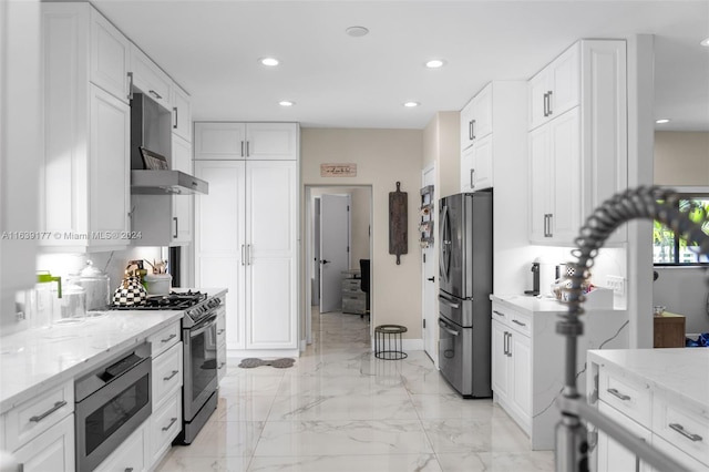 kitchen with light stone counters, appliances with stainless steel finishes, wall chimney range hood, and white cabinets