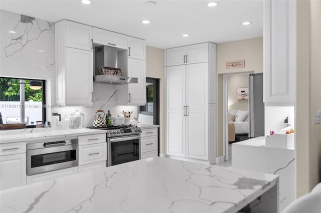 kitchen featuring gas range, wall chimney range hood, white cabinets, and light stone counters