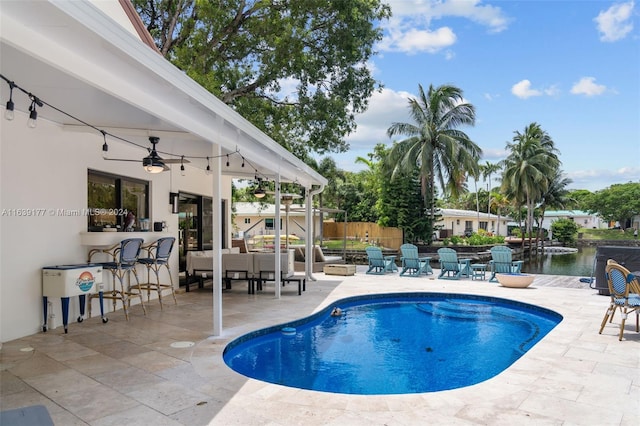 view of pool with a water view, exterior bar, ceiling fan, and a patio area