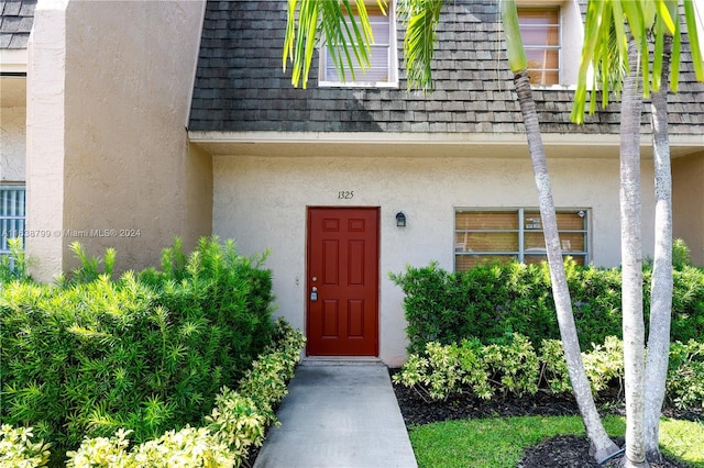 property entrance with roof with shingles, mansard roof, and stucco siding