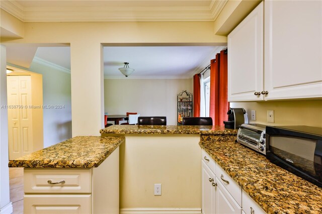 kitchen featuring a toaster, dark stone counters, a peninsula, crown molding, and white cabinetry