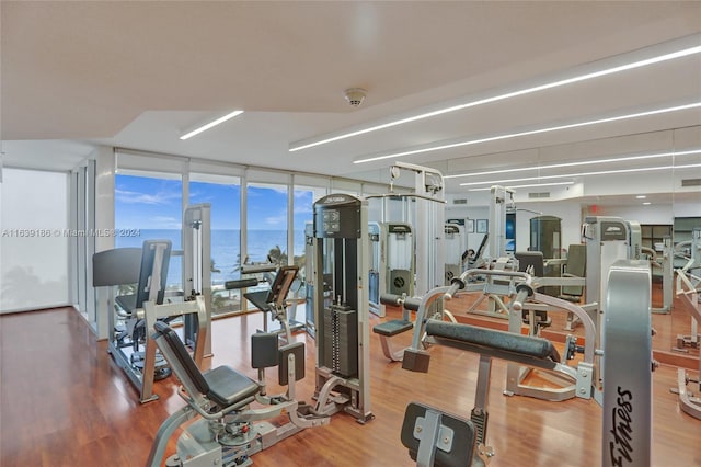 gym with hardwood / wood-style flooring, a wall of windows, and a water view