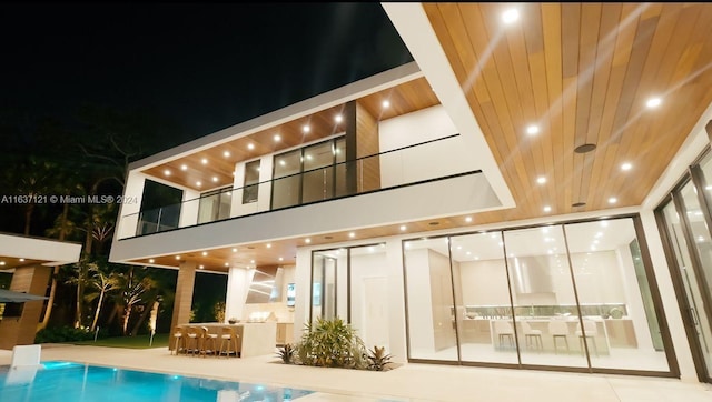 back house at night featuring a balcony and a patio area