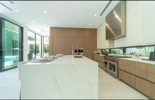 kitchen featuring wall chimney exhaust hood, range with two ovens, white cabinets, and sink