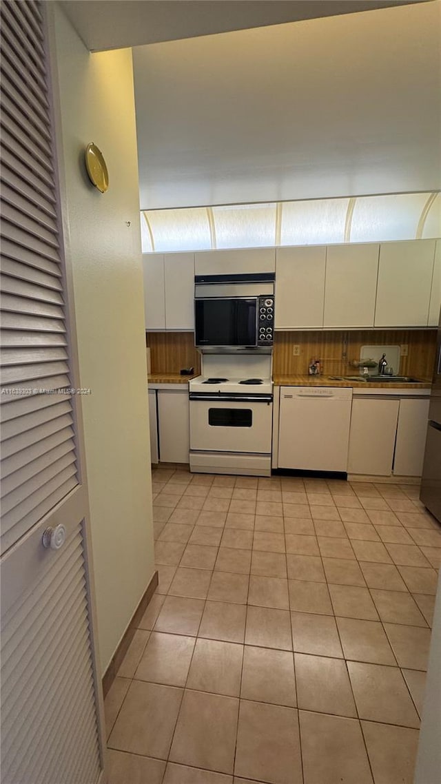 kitchen featuring backsplash, white cabinetry, light tile patterned floors, and white appliances