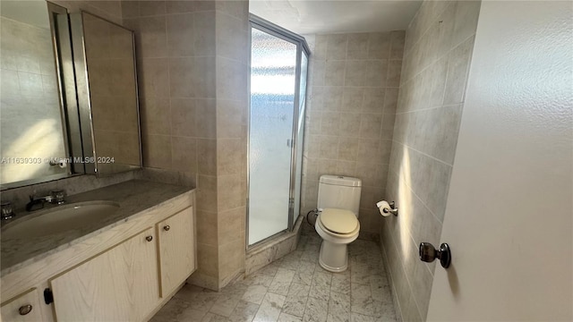 bathroom featuring vanity, toilet, a shower with door, and tile walls