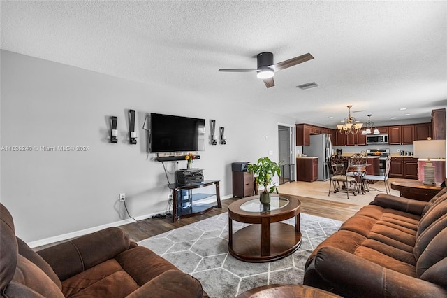 living room with light wood finished floors, visible vents, baseboards, a textured ceiling, and ceiling fan with notable chandelier