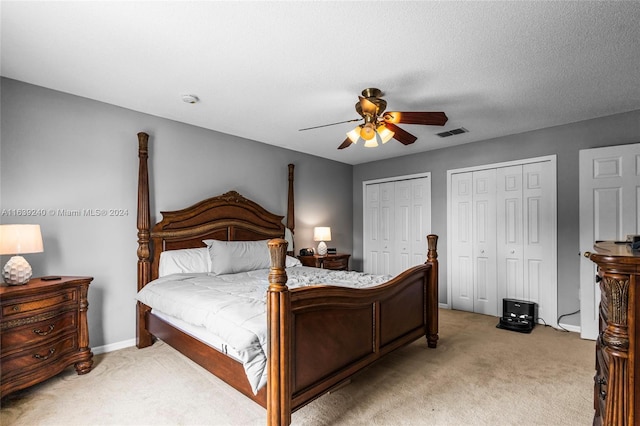 bedroom with ceiling fan, light colored carpet, visible vents, baseboards, and two closets