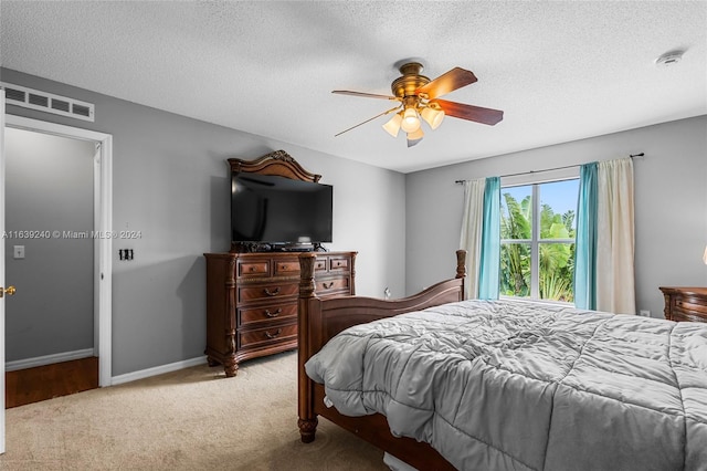 bedroom with a textured ceiling, light colored carpet, a ceiling fan, baseboards, and visible vents