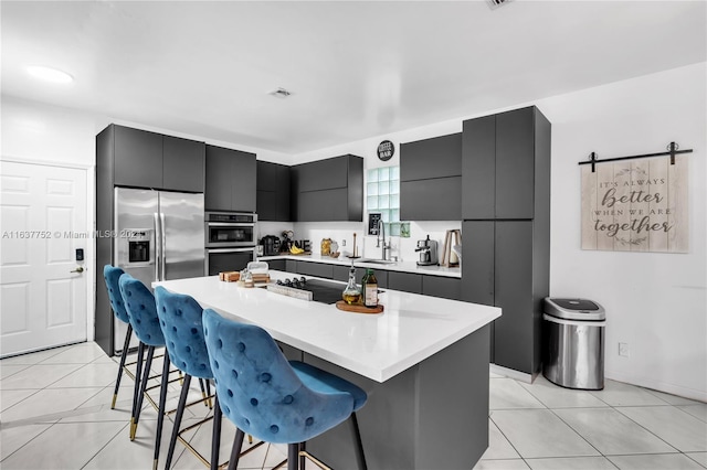 kitchen with a kitchen breakfast bar, stainless steel appliances, a center island, a barn door, and light tile patterned floors