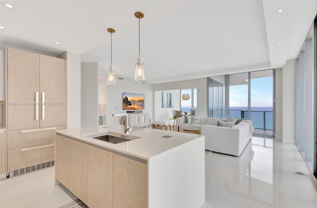 kitchen featuring pendant lighting, light brown cabinets, a kitchen island with sink, light tile patterned floors, and sink