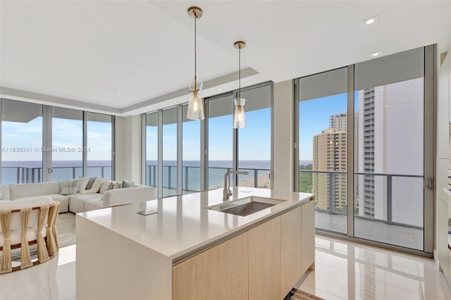 kitchen with light brown cabinetry, a center island with sink, sink, light tile patterned flooring, and a water view