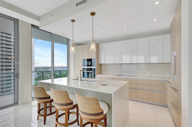 kitchen featuring a center island with sink, stainless steel appliances, sink, light tile patterned floors, and white cabinets