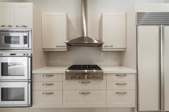 kitchen with decorative backsplash, white cabinetry, wall chimney range hood, and built in appliances