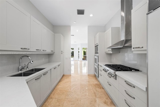 kitchen with appliances with stainless steel finishes, sink, wall chimney range hood, and white cabinetry