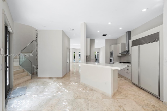 kitchen featuring white cabinets, a kitchen island, wall chimney range hood, gas cooktop, and paneled refrigerator