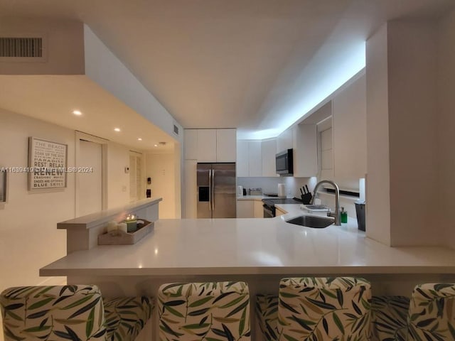 kitchen featuring a breakfast bar area, stainless steel appliances, white cabinetry, sink, and kitchen peninsula