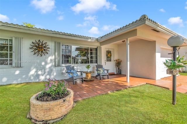 view of exterior entry featuring a patio area and a lawn