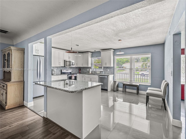 kitchen featuring light stone counters, white cabinets, pendant lighting, light wood-type flooring, and stainless steel appliances