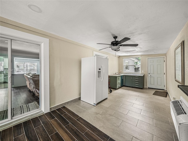 kitchen featuring a textured ceiling, ceiling fan, green cabinetry, white fridge with ice dispenser, and sink