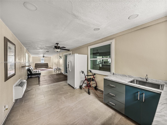 interior space featuring a textured ceiling, ceiling fan, white refrigerator with ice dispenser, light tile patterned floors, and sink