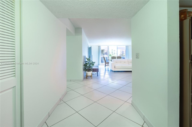 hall featuring a textured ceiling, floor to ceiling windows, and light tile patterned floors