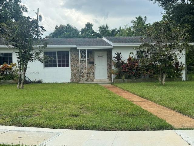 ranch-style home with stucco siding, roof with shingles, and a front yard