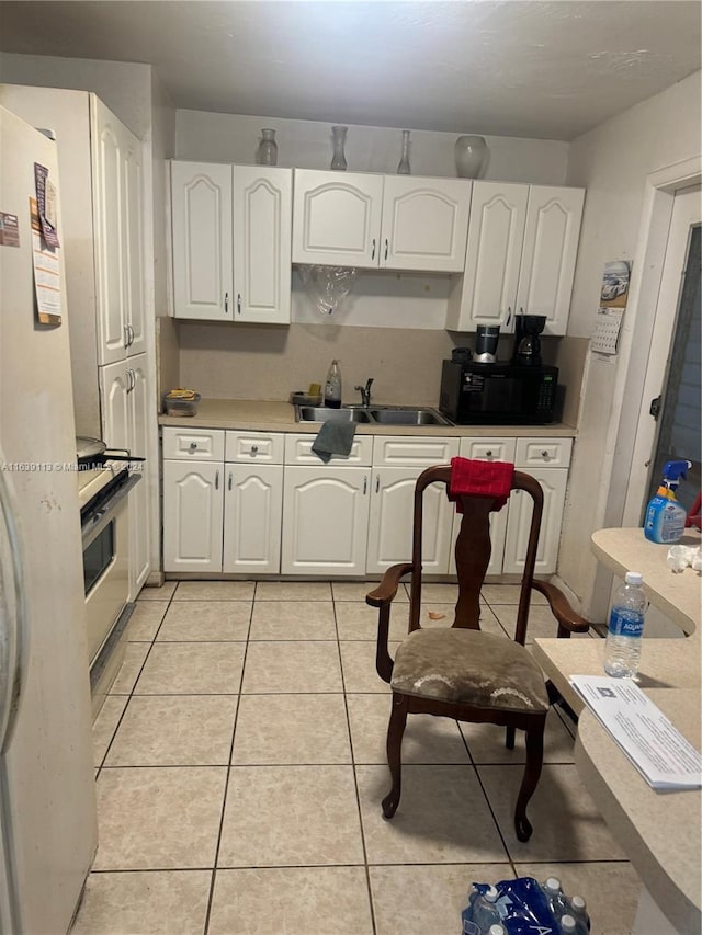 kitchen with black microwave, light tile patterned floors, a sink, white cabinets, and freestanding refrigerator