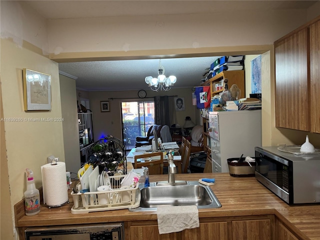 kitchen featuring pendant lighting, sink, dishwasher, an inviting chandelier, and a textured ceiling