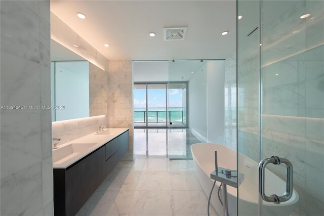 bathroom with vanity, a bath, a water view, a wall of windows, and tile walls